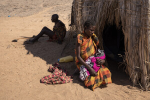 Selina holds her one-week-old daughter Akaru as her father Emanikor rests near the hut where they live in Chok Chok village, located in Turkana County, northwest Kenya on October 14, 2024. Due to the severe drought that is affecting the country, Selina and her family are forced to drink water that they fetches from the nearest river – located about 15 kilometers from their village – which is not clean and often causes infections or diseases, including dysentery, a leading cause of death among children under 5.