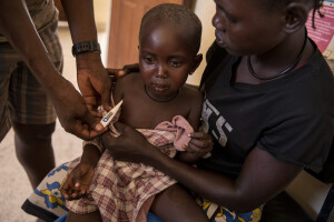 Vivian, 3 years old suffering from malaria cries as a doctor measures her temperature and her mother Gladys holds her in her arms inside the examination room of the Kangatosa Health Centre located in Turkana County, northwest Kenya on October 19, 2024. Little girls often go fetching water with their mothers in areas where stagnant pools of water form and mosquitoes that carry the malaria parasite proliferate. Over the past three years Kenya has suffered from intense drought, partly caused by global warming, which also provides favourable conditions for the development of these mosquitoes.