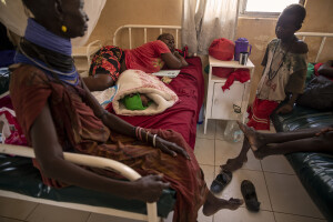 Deborah, 27 years old (center) rests on the bed near her one day old son Bethwel and her mother Nachopu (left), while a little girl (right) watches them at Katilu sub-country hospital located in Turkana County, northwest Kenya on October 18, 2024. Due to the severe drought that is affecting the country, Deborah and her family, including her newborn son, are forced to drink water that they fetch from the underground, which is not clean and often causes infections or diseases, including dysentery, a leading cause of death among children under 5.