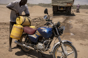 A man attaches canisters of water fetched from the dried Turkwel River to his motorcycle in Chok Chok village, located in Turkana County, northwest Kenya on October 16, 2024. Some people have turned the severe drought that is affecting the country into a real business, selling each 20-litre water tank for 5 Kenyan shillings. However, the water that they fetch from the underground, is not clean and often causes infections or diseases.