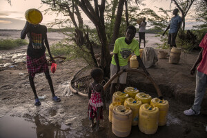 A man (left) drinks water from a canister while another man (right) fills water cans using a mechanical extractor placed on the dried Napasinyang riverbed in Kalokol, located in Turkana County, northwest Kenya on October 15, 2024. Some people have turned the severe drought that is affecting the country into a real business, selling each 20-litre water tank for 5 Kenyan shillings. However, the water that they fetch from the underground, is not clean and often causes infections or diseases.